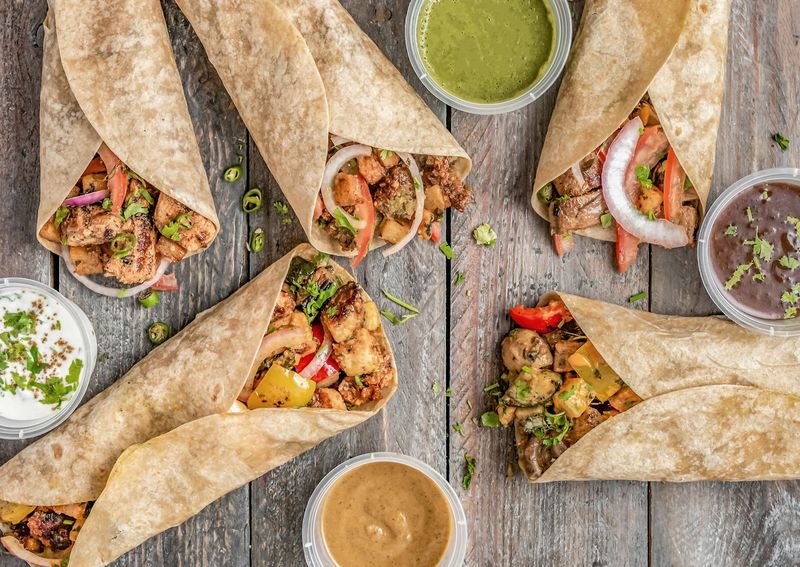 Warm tortilla wraps filled with fully cooked chicken and peppers, with sauces on the side